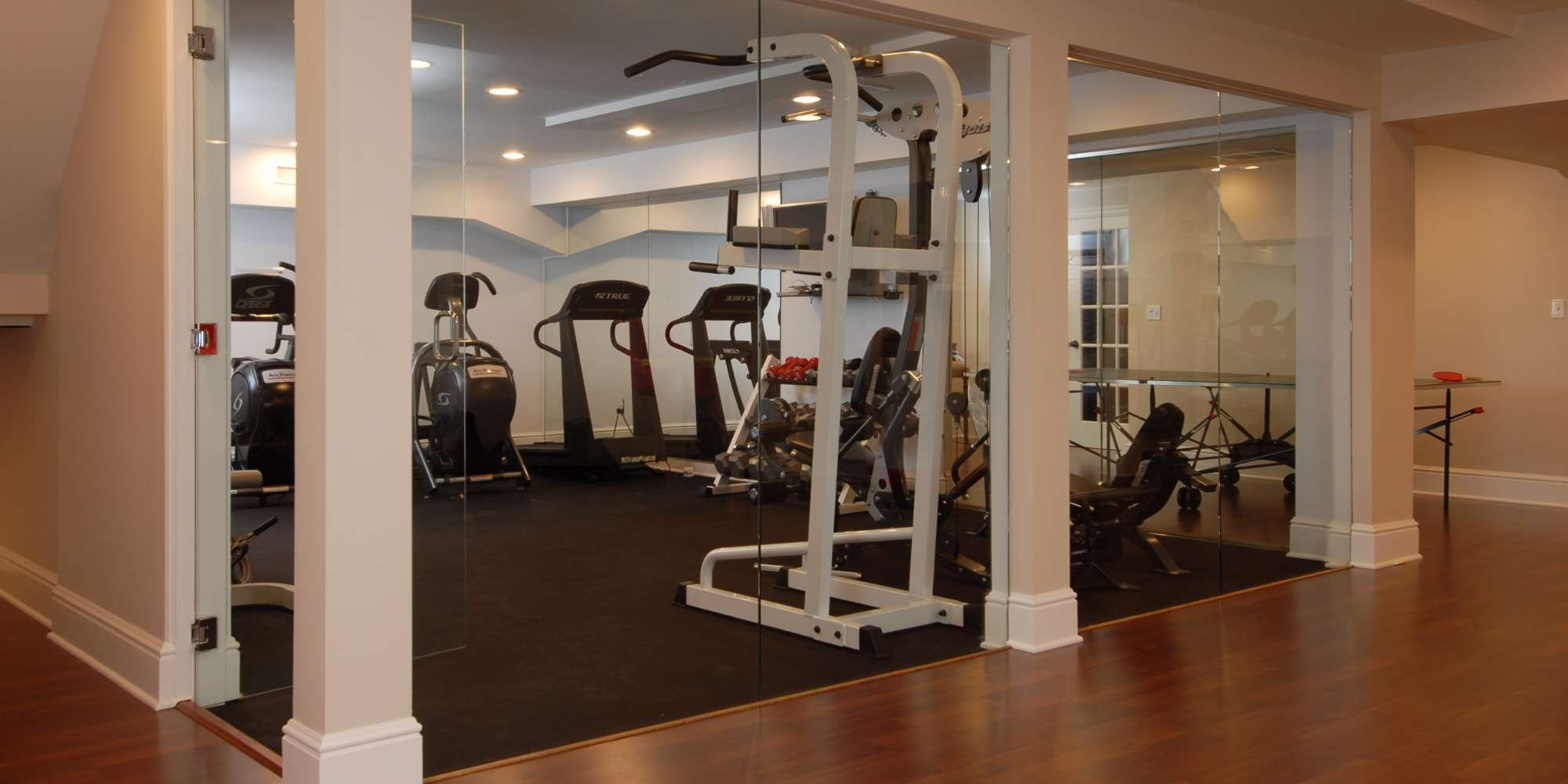 Custom home addition featuring a private fitness room with glass walls, treadmills, and strength equipment by TR Design Build