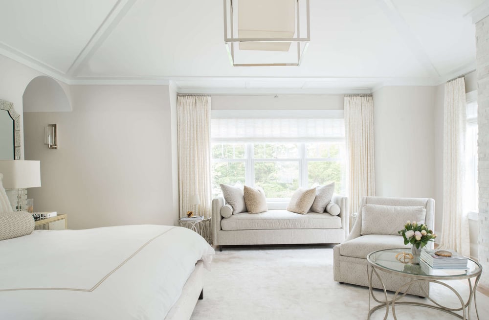 A custom bedroom featuring light-colored walls, carpet, and furniture, with large windows that fill the room with natural light.