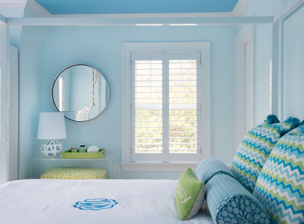 custom bedroom with light blue walls, window, and circular mirror