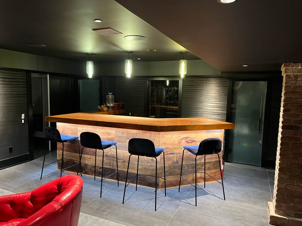 A custom basement bar area featuring a solid wood bar with custom lighting, four seats, and a separate sitting area