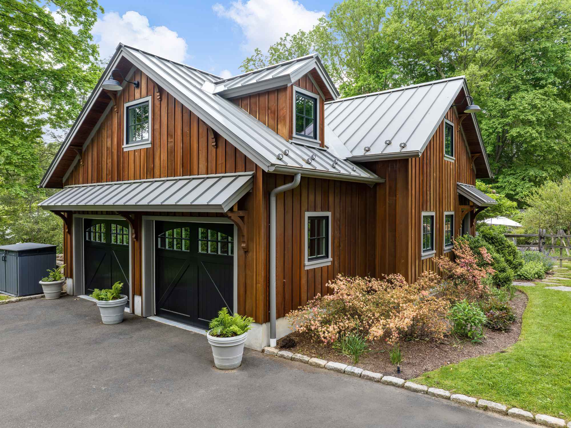 A barn-inspired detached garage accessory structure with a standing-seam metal roof, cedar siding, two garage doors, and a dormer window on the second floor by TR Design-Build in New Canaan, CT A barn-inspired detached garage accessory structure with a standing-seam metal roof, cedar siding, two garage doors, and a dormer window on the second floor by TR Design-Build in New Canaan, CT